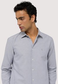 Camicia azzurro chiaro con bottoni, realizzata in tessuto morbido, con colletto all'inglese, bottoni bianchi e un piccolo logo ricamato sul petto.
