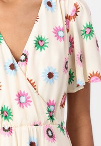 Floral wrap dress with flutter sleeves; features colorful flowers in pink, blue, green, and brown on a cream background. Soft fabric texture.