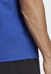T-shirt de sport AEROREADY bleu avec une texture lisse, des manches courtes et un logo subtil en bas, associé à un short noir.