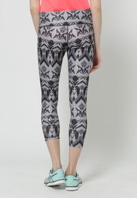 Černé a šedé legíny s vzory, vysokým pasem, zkráceným střihem a hladkou texturou. Nosené s světle modrými sportovními botami.