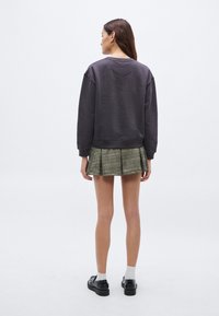 Hanorac gri cu decolteu rotund, mâneci lungi și manșete rib, asortat cu o fustă plisată în carouri. Pantofi negri și șosete vizibile.