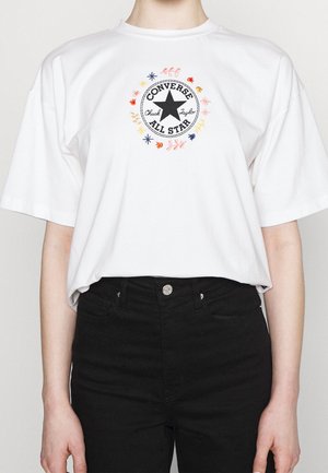 Camiseta blanca de manga corta con un diseño circular bordado que incluye una estrella negra en el centro y detalles florales multicolores.