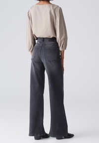 Top de manga abullonada en beige claro combinado con jeans de pierna ancha de tiro alto en gris oscuro, con dos bolsillos traseros y una textura lisa de mezclilla.