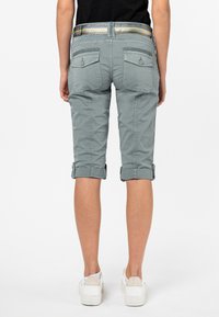 Groene cropped broek met opgerolde mouwen, met achterzakken met knoopflappen. Gecombineerd met witte sneakers voor een casual look.