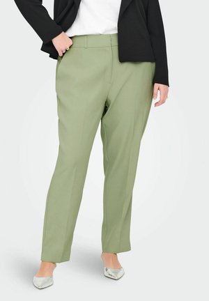 Pantaloni su misura verde chiaro con design a gamba dritta. Il materiale appare liscio con una leggera lucentezza. Abbinati a un blazer nero e scarpe argentate.