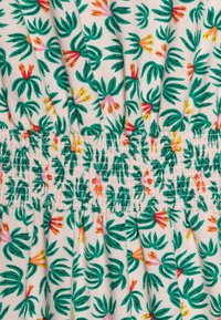 Bílá tkanina se květinovým vzorem s výraznými zelenými listy a vícebarevnými květinami v červené, žluté a růžové barvě. Přítomný detail nařaseného smocking.