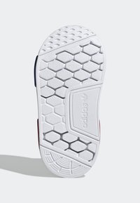 Vit gummisula med hexagonal textur, med ett slätt centralt område och Adidas-logotyp på ena sidan. Accenterad med röda och blå kanter.