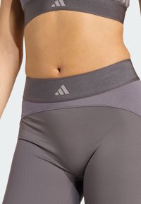 Close-up središnjeg dijela tijela u ljubičastom Adidas sportskom bh-u i tajicama s logotipom na elastičnim pojasovima.