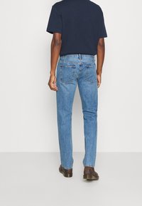 Vaqueros de mezclilla azul con un corte holgado, que cuentan con bolsillos estándar, detalles sutíles de costura y diseño de pierna recta. Zapatos de cuero marrón visibles.