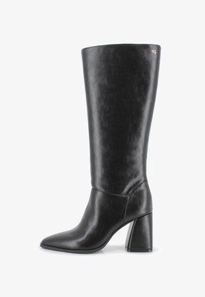 Bota de cuero negra hasta la rodilla con punta afilada y tacón cuadrado, que presenta un pequeño logo metálico de la marca cerca del borde superior.