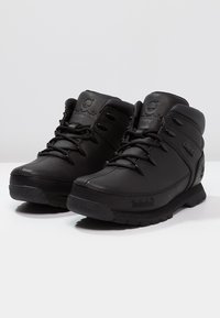 Botas de senderismo de cuero negro con un diseño de media caña, que cuentan con costuras reforzadas, cierre con cordones y suelas de goma texturizada.