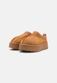 Zapatos tipo mocasín de ante en color tostado con un acento de punto colorido y texturizado en el cuello. Presenta una suela de goma gruesa y texturizada.