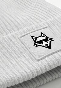 Light gray knit beanie with a ribbed texture and a rectangular badge featuring a black wolf logo wearing sunglasses.