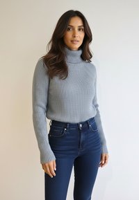 Szary prążkowany golf z długimi rękawami, zestawiony z ciemnoniebieskimi, wysokim stanem dżinsami. Gładka faktura, dopasowany krój.