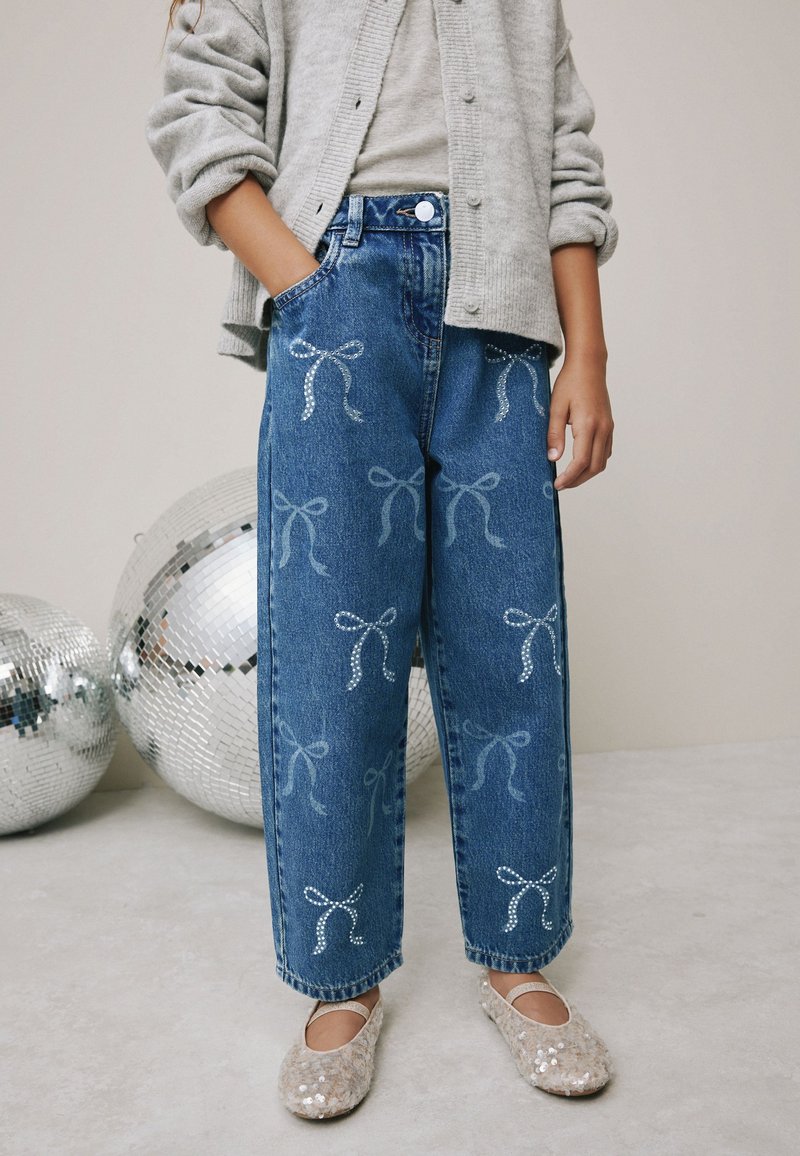 Jeans in denim a vestibilità ampia, con motivi a fiocco azzurro chiaro e paillettes argento. Indossati con un cardigan grigio e ballerine beige scintillanti.