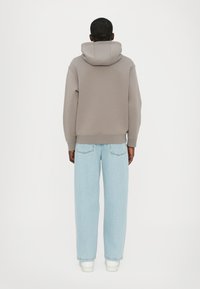 Felpa grigia con cappuccio dal design rilassato, abbinata a jeans blu chiaro a gamba dritta, con due tasche posteriori e sneakers bianche.