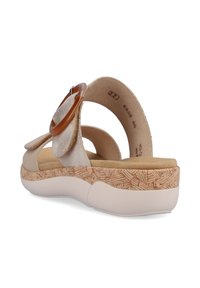 Sandale beige clair avec un dessus en suède, une sangle réglable, un grand accent rond en tan et une semelle texturée ressemblant à du liège pour un soutien.