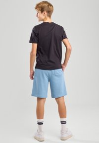 T-shirt en coton noir à col rond, associé à un short bleu clair avec une taille élastique et une poche arrière. Agrémenté de chaussettes rayées blanches et bleu marine et de baskets blanches.