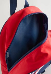 Mochila roja y azul marino con un exterior suave y duradero y un interior espacioso, que cuenta con un cierre de cremallera y forro de tela.