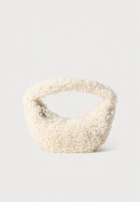 Bolsa de cor creme, felpuda, feita de tecido texturizado, com alça curva e pequeno pendente de log ótipo para detalhe.