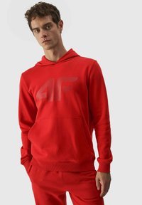 Sudadera con capucha roja con un gran logo reflectante "4F". Cuenta con un bolsillo delantero y puños acanalados, hecha de una tela suave y suave.