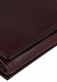 Portefeuille en cuir bordeaux avec une texture lisse, design plié et couture contrastée. Dispose de coins arrondis et d'un profil élégant.
