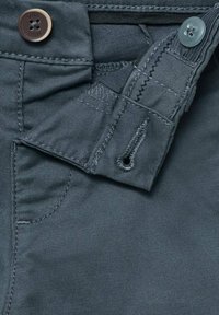 Tmavě šedé kalhoty s knoflíkovým zapínáním, mají zip a poutka na opasek. Materiál má hladký, texturovaný povrch s viditelnými detaily šití.