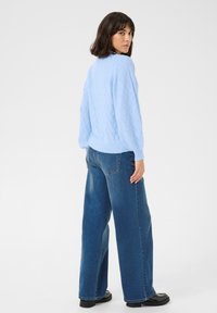Pull en tricot bleu clair avec un motif texturé, associé à un jean bleu taille haute et à jambe large, ainsi qu'à des chaussures noires. Tricot doux et coupe décontractée.