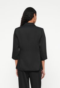 Blazer negro con mangas tres cuartos, diseño entallado y cuello con solapa. Textura lisa y mate con líneas limpias y sin cierres visibles.