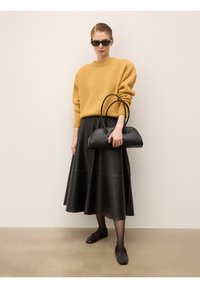 Suéter de punto amarillo, falda midi de cuero negra, bolso negro con diseño curvado y zapatos planos negros. Las gafas de sol añaden un toque moderno.