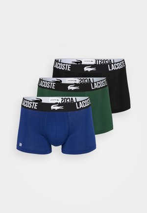 Drie paar Lacoste boxershorts in blauw, groen en zwart. Elk met een elastische tailleband met het Lacoste-logo en een klassieke pasvorm.