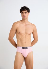 Men's brief underwear in light pink, made of soft fabric, with a black elastic waistband featuring the logo "DIESEL" prominently displayed.