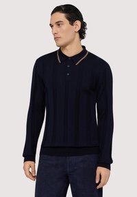Námořnická modrá polo košile s dlouhým rukávem, vertikálně ribbovanou texturou, tříknoflíkovou légou a kontrastními béžovými akcenty na límci.