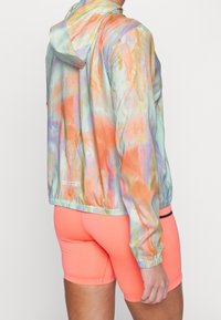 Kapucové větrové sako v barevném pastelovém tie-dye s texturovaným povrchem; elastický pas a manžety. Spárováno s jasně růžovými šortkami.