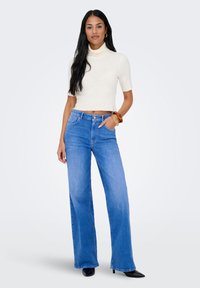 Kreminės spalvos ribuotas trumpomis rankovėmis golfas, derinamas su šviesiai mėlynais plačiomis kojomis džinsais, turinčiais priekinės kišenes ir sagų užsegimą. Juodi aukštakulniai batai.