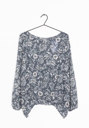 Graue Langarmbluse mit weißen Blumen- und Schmetterlingsmustern, an einem schwarzen Drahtbügel hängend vor weißem Hintergrund.