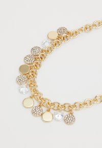 Gold chain necklace featuring alternating circular pendants, some with clear rhinestones, others smooth, creating a textured pattern.