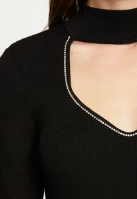 Haut noir côtelé avec un col haut et un décolleté en V, accentué par une rangée de petits strass le long du bord.