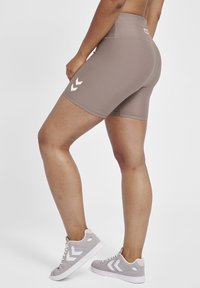 Brown athletic shorts with a high waist, smooth texture, featuring white chevron accents on the side, paired with gray sneakers.