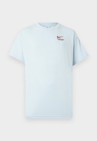 Gaiši zils kokvilnas T-krekls ar īsām piedurknēm, apaļu kaklu un sarkano Nike swoosh logo. Uzraksts: "SPORTA NODAĻA. TIKAI DARI TO."