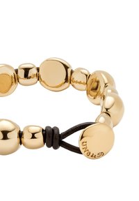 Pulsera de cuentas de color dorado con formas esféricas variadas, que cuenta con un cordón de cuero y un pequeño adorno metálico con un logo grabado.