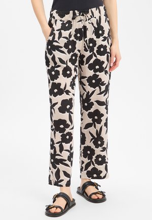 Beige broek met grote zwarte bloemenprint, elastische tailleband met trekkoord, gedragen met zwarte sandalen en een zwart topje.