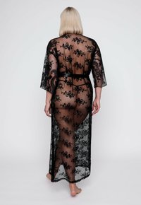 Zwarte kant kimono met bloemgeborduurde details, transparante stof, driekwartmouwen en een strikceintuur in de taille, die de silhouette accentueert.