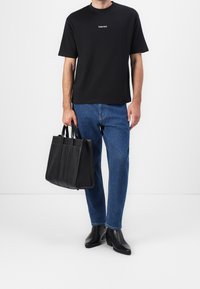 Black short-sleeve t-shirt with white "Selected" logo, blue denim jeans, black leather handbag with handles, and shiny black shoes.