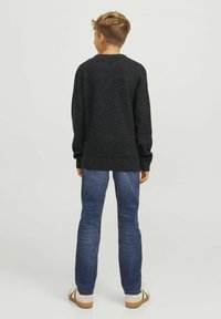 Pull noir à manches longues en tissu texturé, avec des poignets et un ourlet côtelés, associé à un jean bleu et des chaussures blanches avec des accents verts.