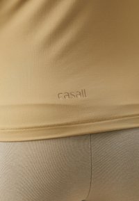 Maglietta atletica beige con texture liscia, maniche corte e discreto logo "casall" sull'orlo. Abbinata a pantaloni aderenti beige coordinati.