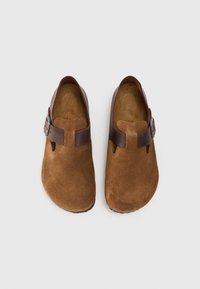 Braune Wildlederschuhe zum Hineinschlüpfen in runder Form mit einem dunkelbraunen Riemen und silbernem Schnallen-Detail sowie einer strukturierten Innensohle.