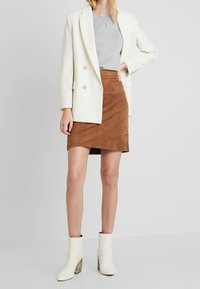 Blazer blanco de doble botonadura sobre una camiseta gris, combinado con una falda corta de ante marrón y botas blancas hasta el tobillo con un tacón de bloque estampado.