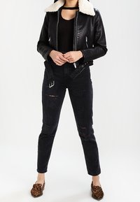 Schwarze Lederbomberjacke mit einem weißen Schaffellkragen, schwarze enganliegende Jeans mit Rissen und braune Loafers im Leopardenmuster.