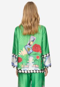 Giacca in raso verde con un design colorato di fiori e carte dei tarocchi, con accenti geometrici neri sulle maniche e sull'orlo.